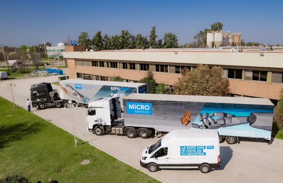 Camiones y camioneta de la exposición móvil de MICRO estacionados frente a una planta